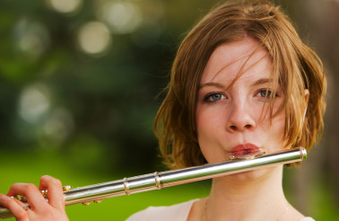 A pretty teen playing her flute outside